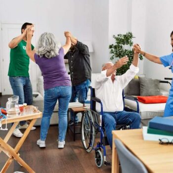 Group of retired people having party dancing with doctor and volunteer at nurse home.