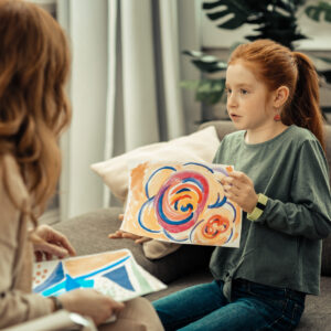 A creative music therapy session in Melbourne, with a young girl showing a drawing to a woman.