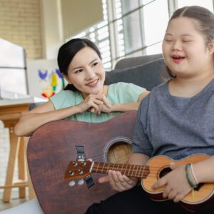 A music therapy session in Melbourne with a young woman playing a ukulele accompanied by a woman with a guitar.