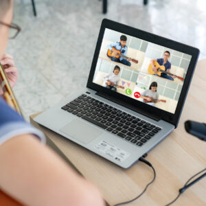 Online music therapy session based in Melbourne. A boy is playing guitar with other people online.